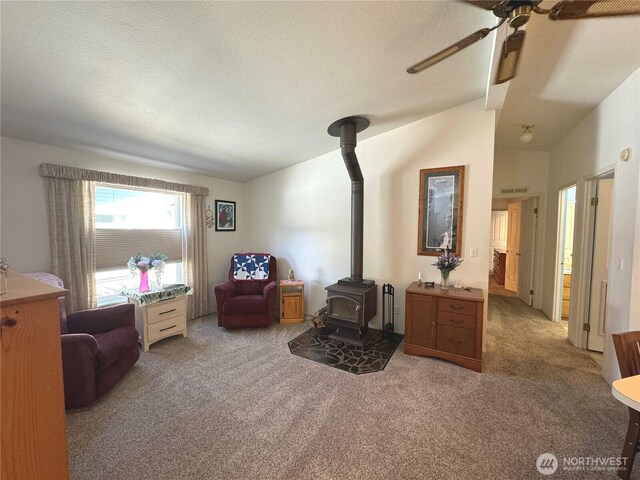 living area with a textured ceiling, carpet, a wood stove, and a ceiling fan