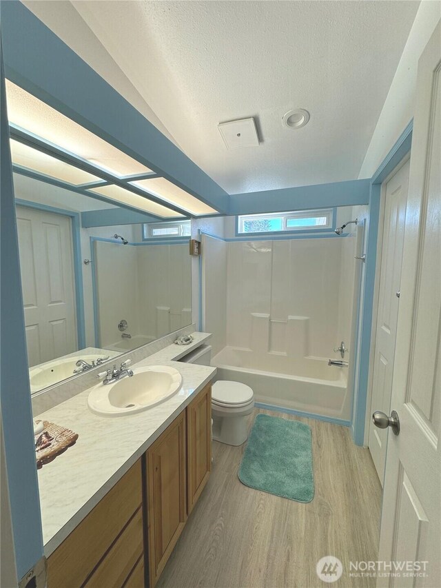 full bathroom with toilet, vanity, shower / bathtub combination, wood finished floors, and a textured ceiling