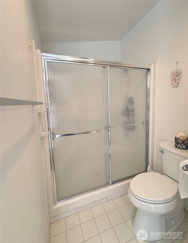 bathroom featuring lofted ceiling, toilet, tile patterned flooring, and a shower stall