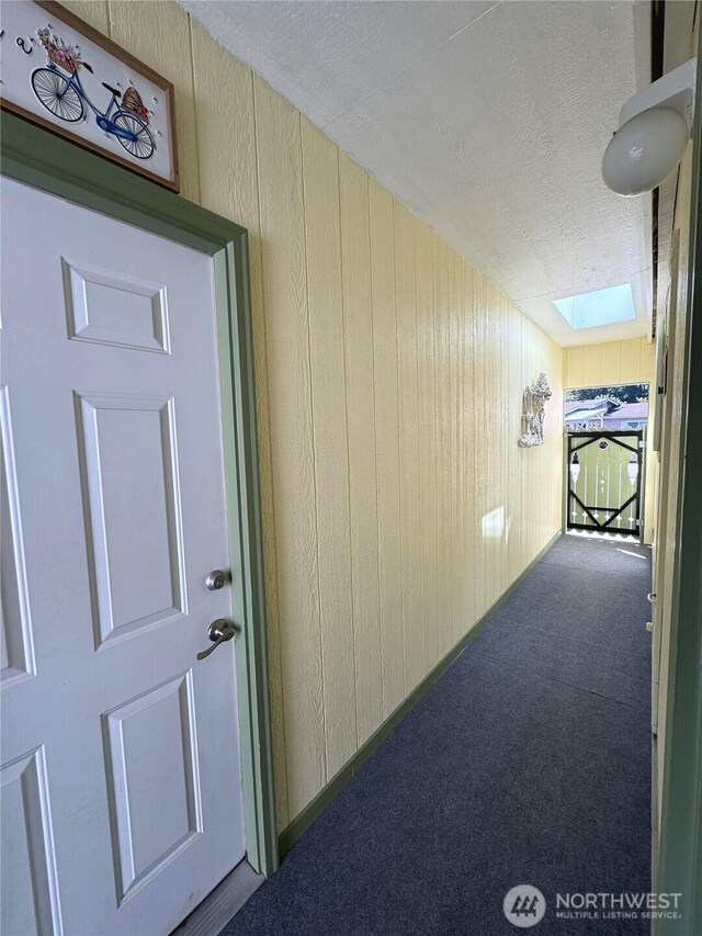 hall with a skylight, carpet, a textured ceiling, and wood walls