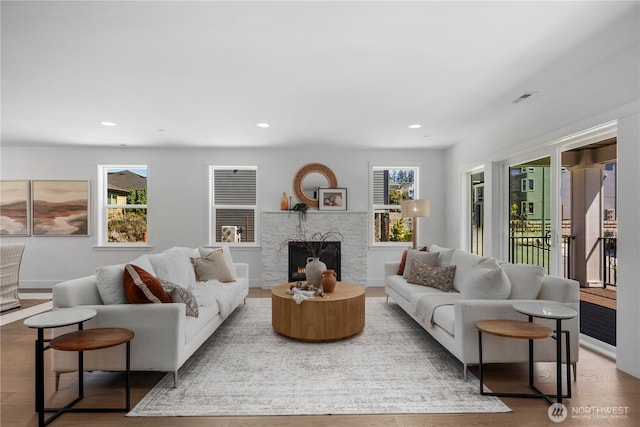 living room featuring plenty of natural light, recessed lighting, a warm lit fireplace, and baseboards