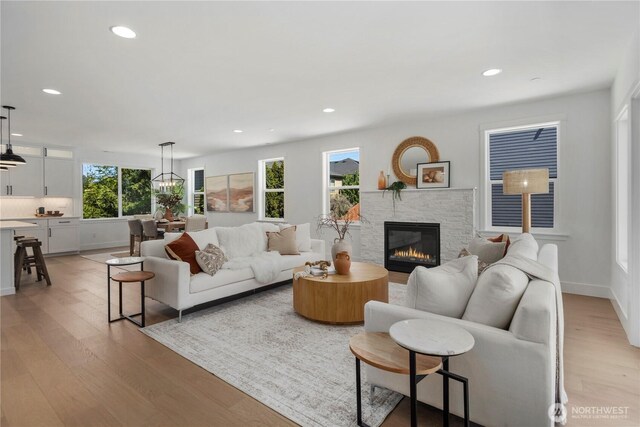 living area featuring light wood-style flooring, a stone fireplace, recessed lighting, and baseboards