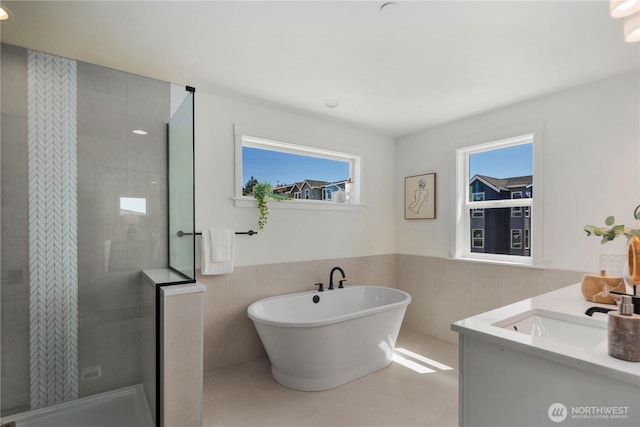 full bath featuring tile walls, a tile shower, healthy amount of natural light, a freestanding bath, and a wainscoted wall