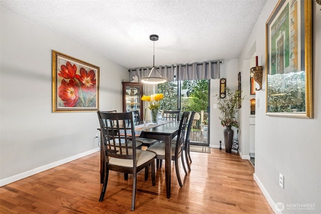 dining space with light wood-style flooring, a textured ceiling, and baseboards