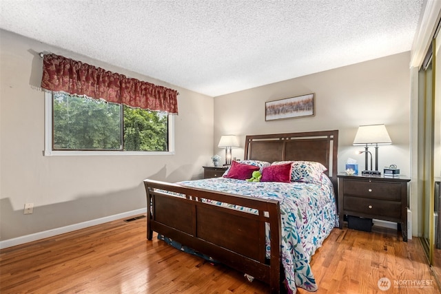 bedroom featuring a textured ceiling, wood finished floors, baseboards, and visible vents