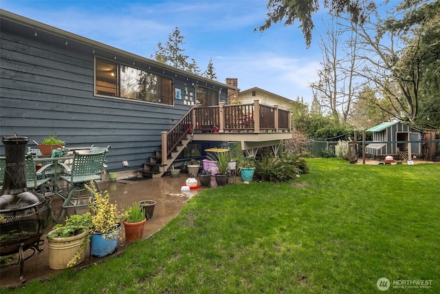 rear view of house featuring a deck, a lawn, fence, stairs, and an outbuilding