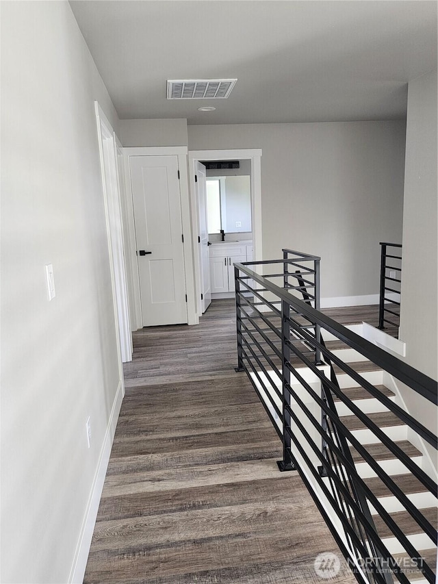 hall featuring dark wood-style flooring, an upstairs landing, baseboards, and visible vents