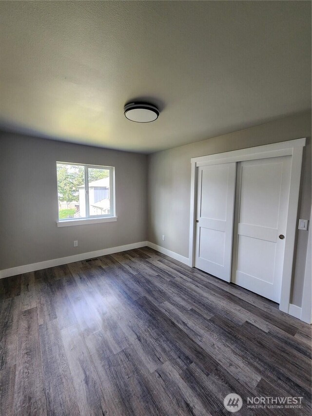 unfurnished bedroom featuring dark wood-style floors, a closet, and baseboards