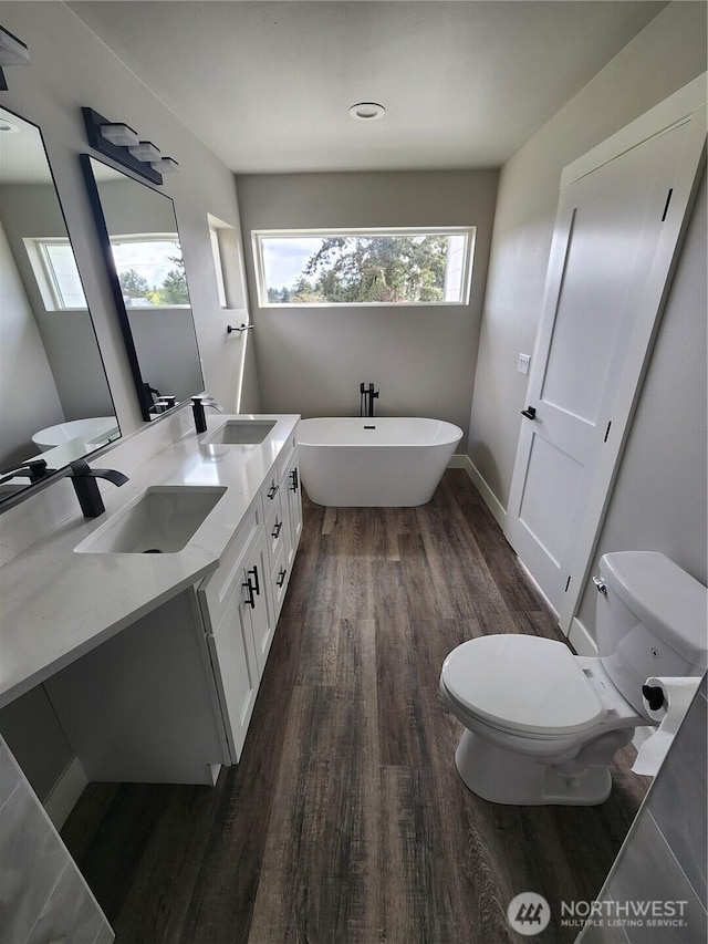 full bathroom featuring a freestanding tub, a sink, toilet, and wood finished floors