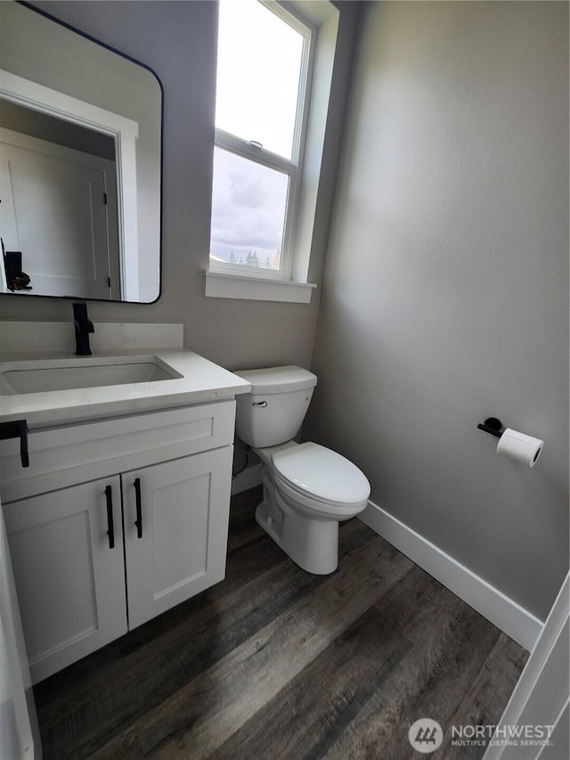 half bathroom featuring baseboards, toilet, vanity, and wood finished floors
