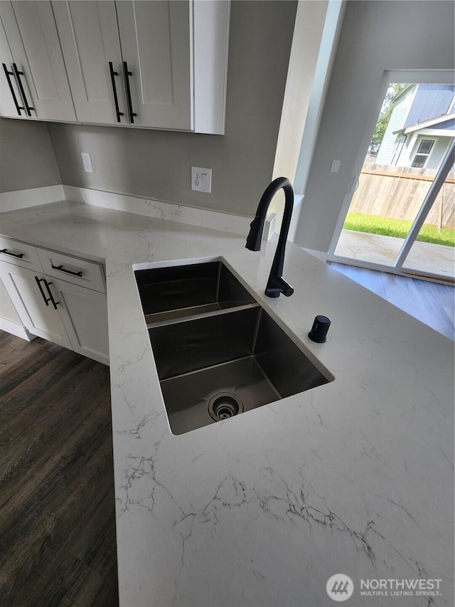 kitchen with white cabinetry, a sink, dark wood-type flooring, and light stone countertops