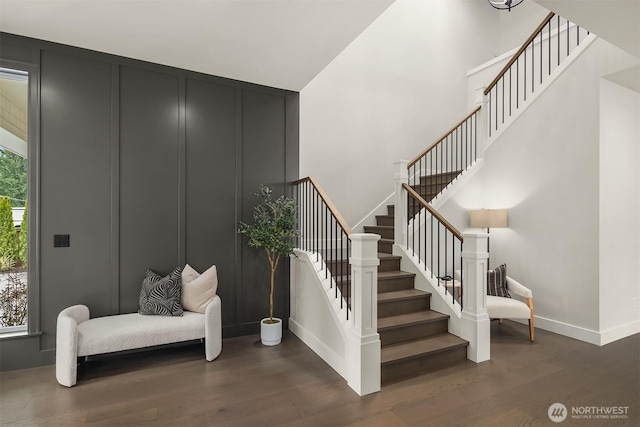 staircase featuring baseboards, a high ceiling, a decorative wall, and wood finished floors