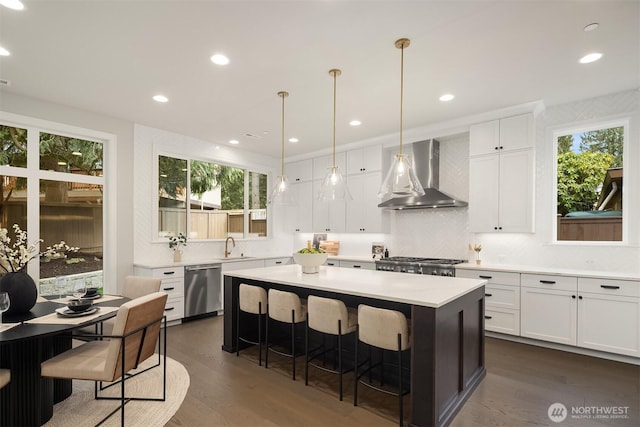 kitchen with light countertops, dishwasher, a kitchen bar, a kitchen island, and wall chimney range hood