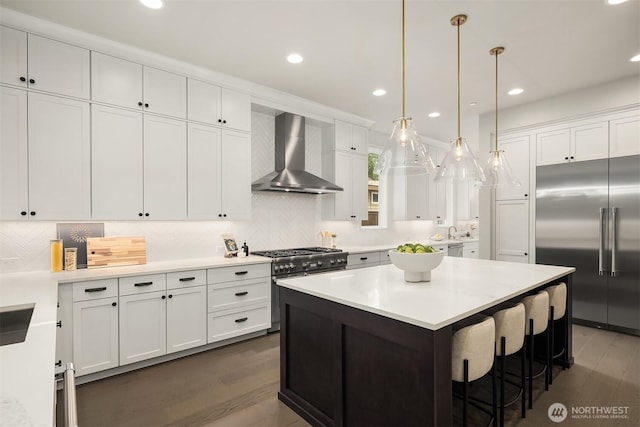 kitchen featuring wall chimney range hood, white cabinets, a center island, and premium appliances