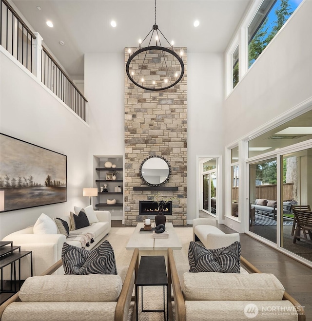 living area featuring a fireplace, wood finished floors, a towering ceiling, recessed lighting, and an inviting chandelier