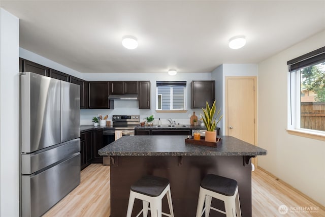 kitchen with appliances with stainless steel finishes, dark countertops, a kitchen breakfast bar, and light wood-style flooring
