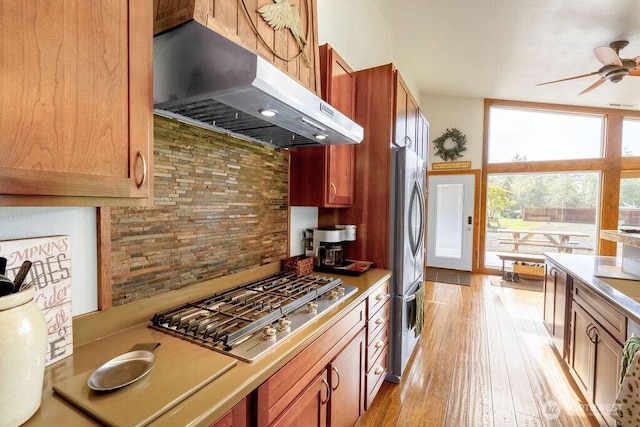 kitchen with decorative backsplash, light wood-style floors, a ceiling fan, appliances with stainless steel finishes, and ventilation hood