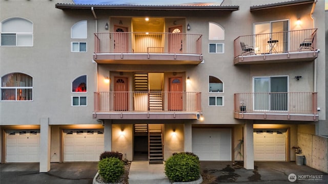 view of property featuring an attached garage, a balcony, stucco siding, and driveway