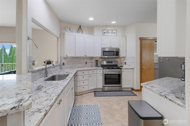 kitchen featuring appliances with stainless steel finishes, tasteful backsplash, light stone countertops, a sink, and white cabinets