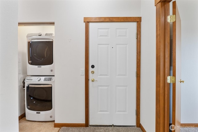 clothes washing area featuring baseboards, stacked washer and dryer, and laundry area
