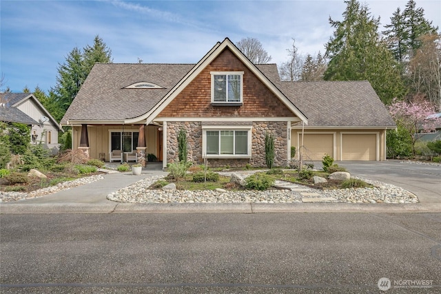 craftsman-style house with a garage, a porch, a shingled roof, stone siding, and driveway