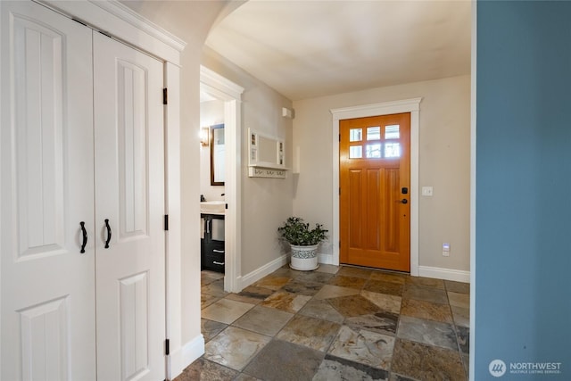 entryway with baseboards, arched walkways, and stone tile floors