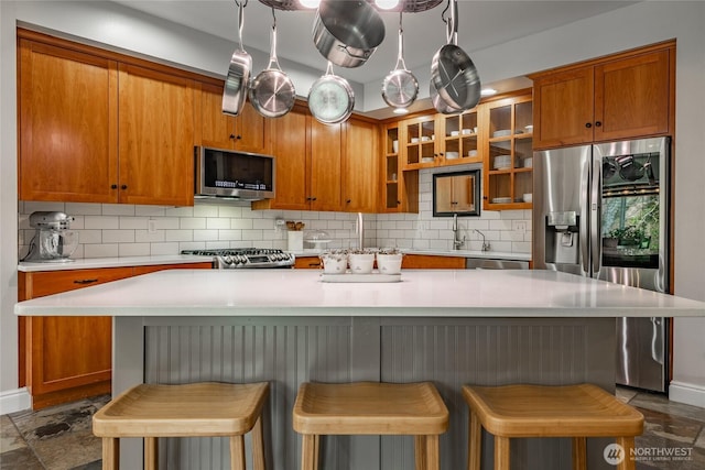 kitchen featuring light countertops, brown cabinetry, backsplash, and appliances with stainless steel finishes
