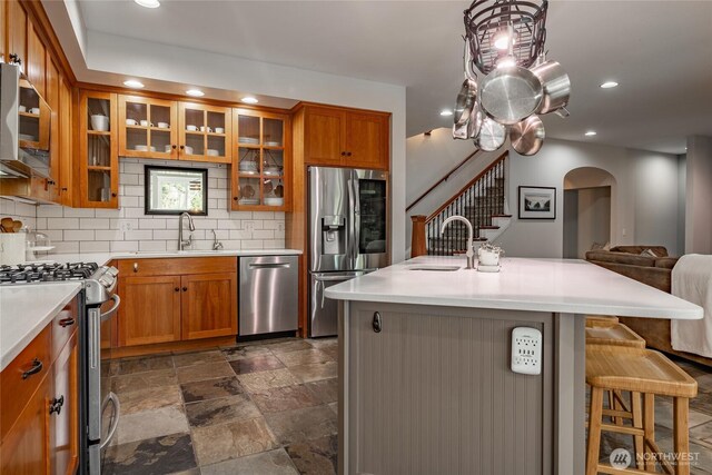 kitchen featuring light countertops, backsplash, brown cabinets, appliances with stainless steel finishes, and a sink