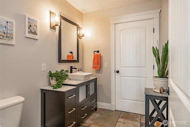 half bathroom with stone tile flooring, toilet, vanity, and baseboards