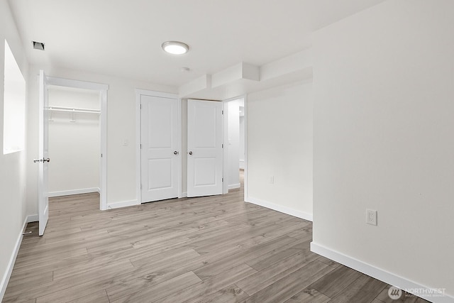 unfurnished bedroom featuring a spacious closet, a closet, baseboards, and light wood-style floors