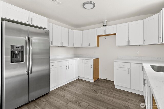 kitchen with dark wood-style flooring, white cabinets, visible vents, and stainless steel fridge
