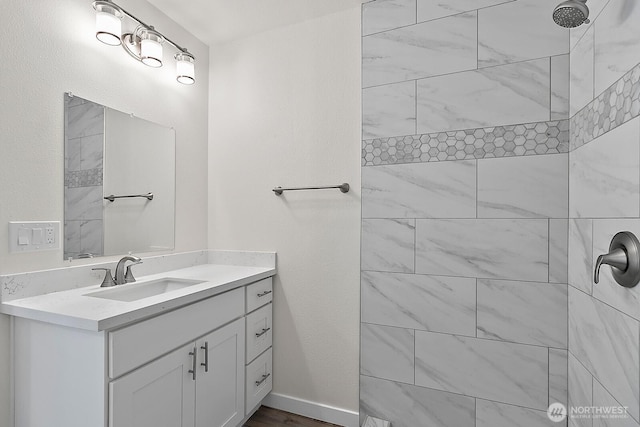 full bath with baseboards, a tile shower, and vanity