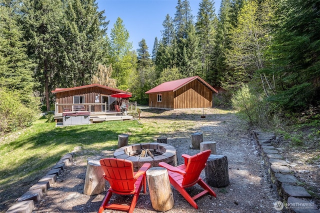 view of grassy yard featuring an outdoor fire pit, a wooded view, a deck, and an outdoor structure