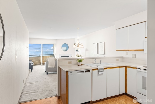 kitchen featuring white cabinets, light countertops, a peninsula, white appliances, and a sink