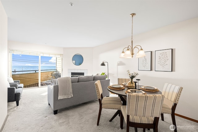dining area featuring baseboards, an inviting chandelier, a tiled fireplace, and light carpet