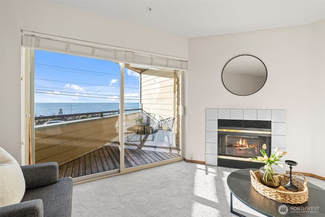 carpeted living room with baseboards, a water view, and a tiled fireplace