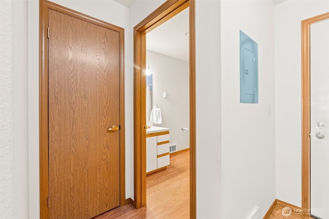 corridor with visible vents, baseboards, light wood-style floors, and electric panel