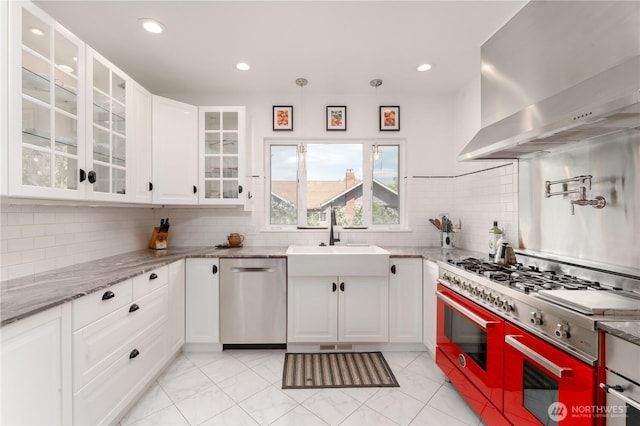 kitchen featuring stainless steel dishwasher, wall chimney exhaust hood, white cabinetry, a sink, and double oven range