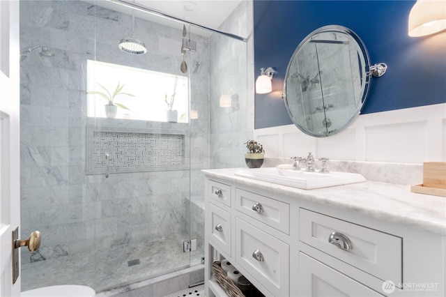 bathroom with toilet, a shower stall, a wainscoted wall, and vanity