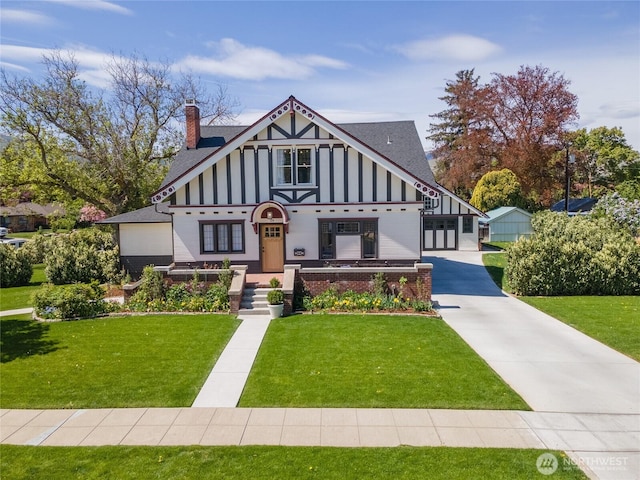 tudor home featuring roof with shingles, board and batten siding, a chimney, and a front lawn