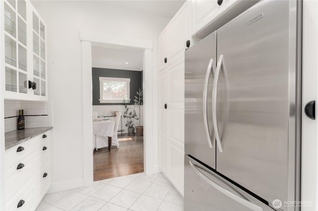 kitchen featuring freestanding refrigerator, decorative backsplash, glass insert cabinets, white cabinetry, and light stone counters