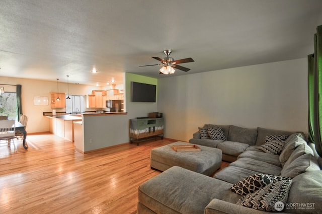 living area featuring light wood-type flooring, ceiling fan, and baseboards
