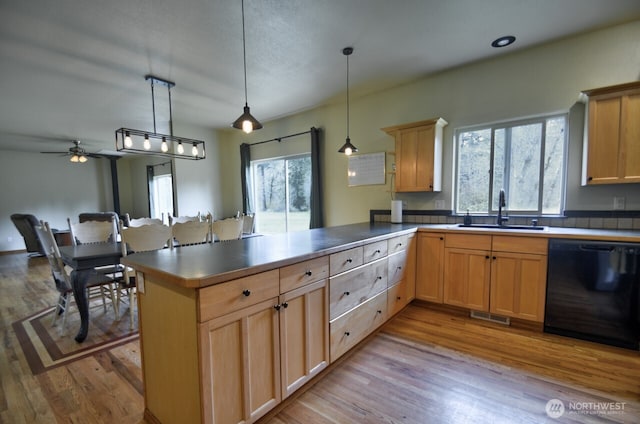 kitchen with light wood-style flooring, a peninsula, visible vents, black dishwasher, and a sink