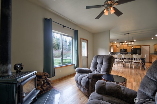 living room featuring a wood stove, a ceiling fan, and light wood-style floors