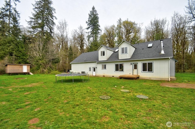 rear view of house featuring a yard, a trampoline, a deck, and roof with shingles