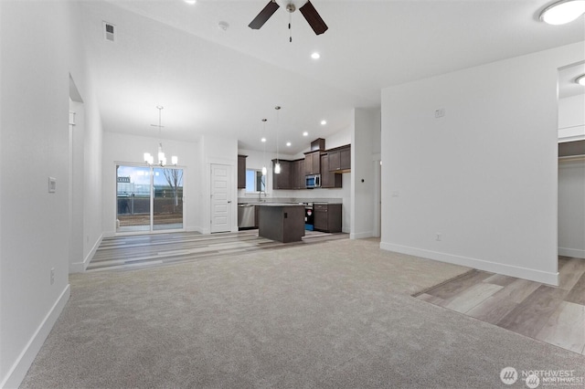 unfurnished living room featuring light carpet, ceiling fan with notable chandelier, and baseboards