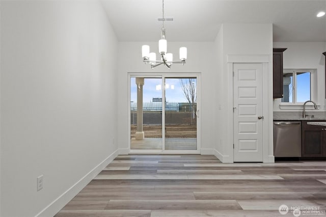 unfurnished dining area with light wood-type flooring, baseboards, a chandelier, a sink, and visible vents