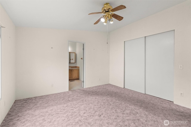 unfurnished bedroom featuring a closet, ensuite bathroom, a ceiling fan, and carpet floors