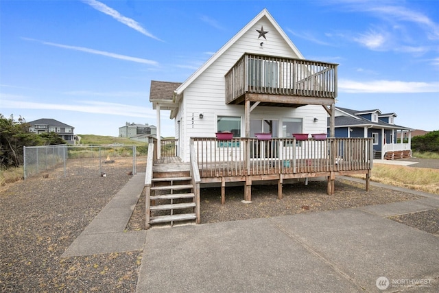 view of front facade featuring a shingled roof, a deck, and fence