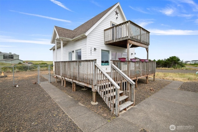 rear view of house featuring a gate, fence, a wooden deck, and roof with shingles